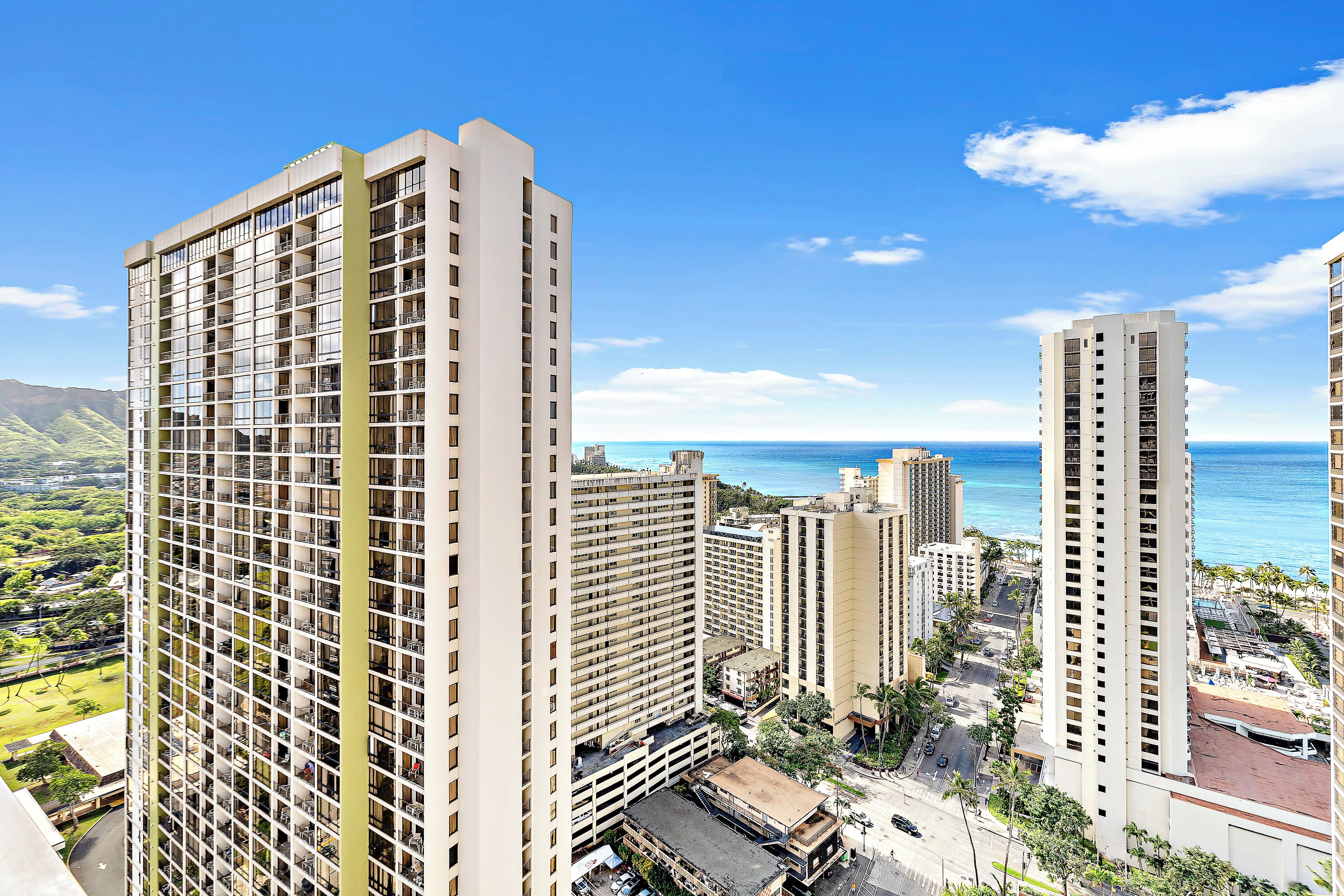 A high-rise hotel with multiple floors, a parking area, and a view of the ocean.