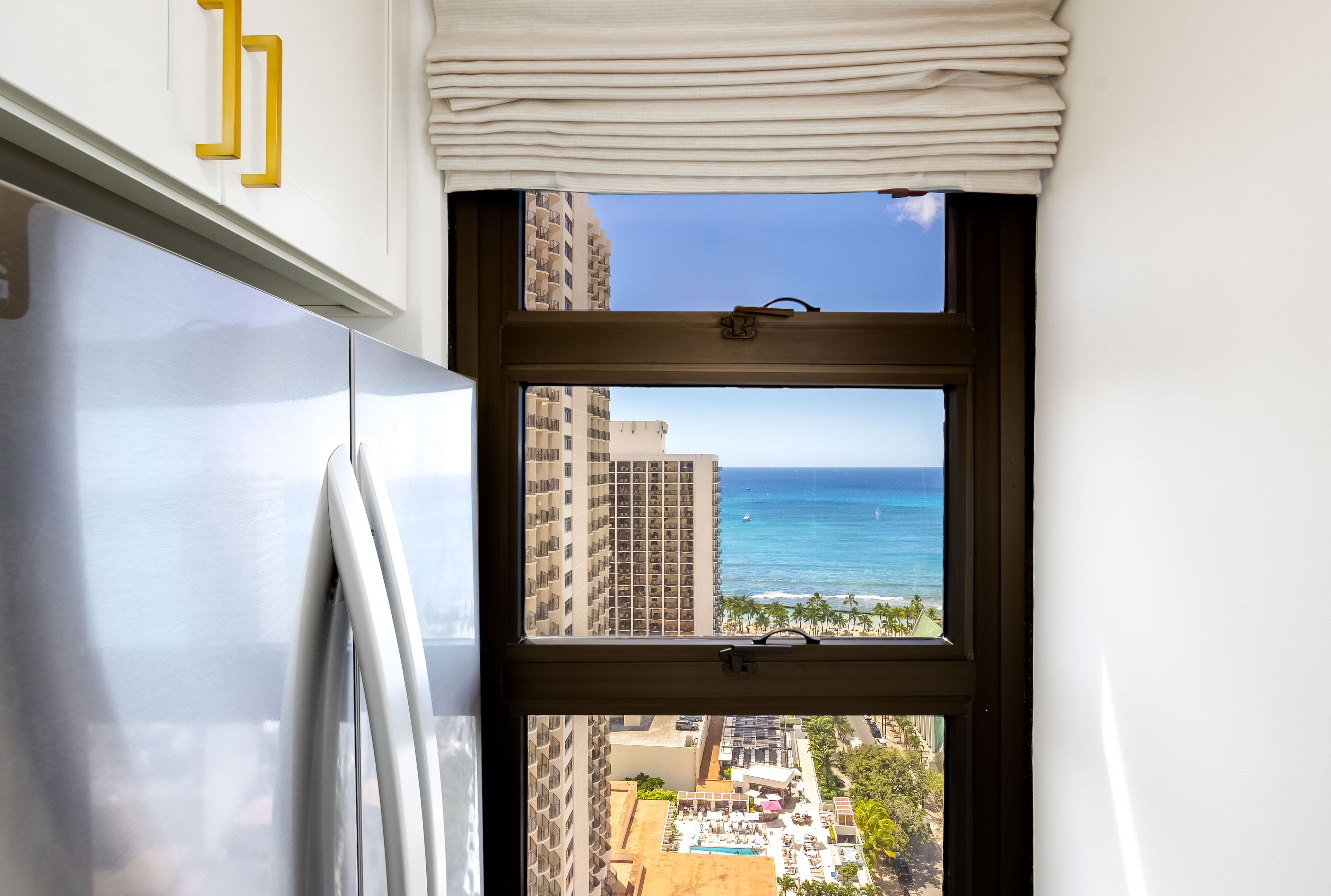 A window view of a high-rise building with a pool and beach in the background.