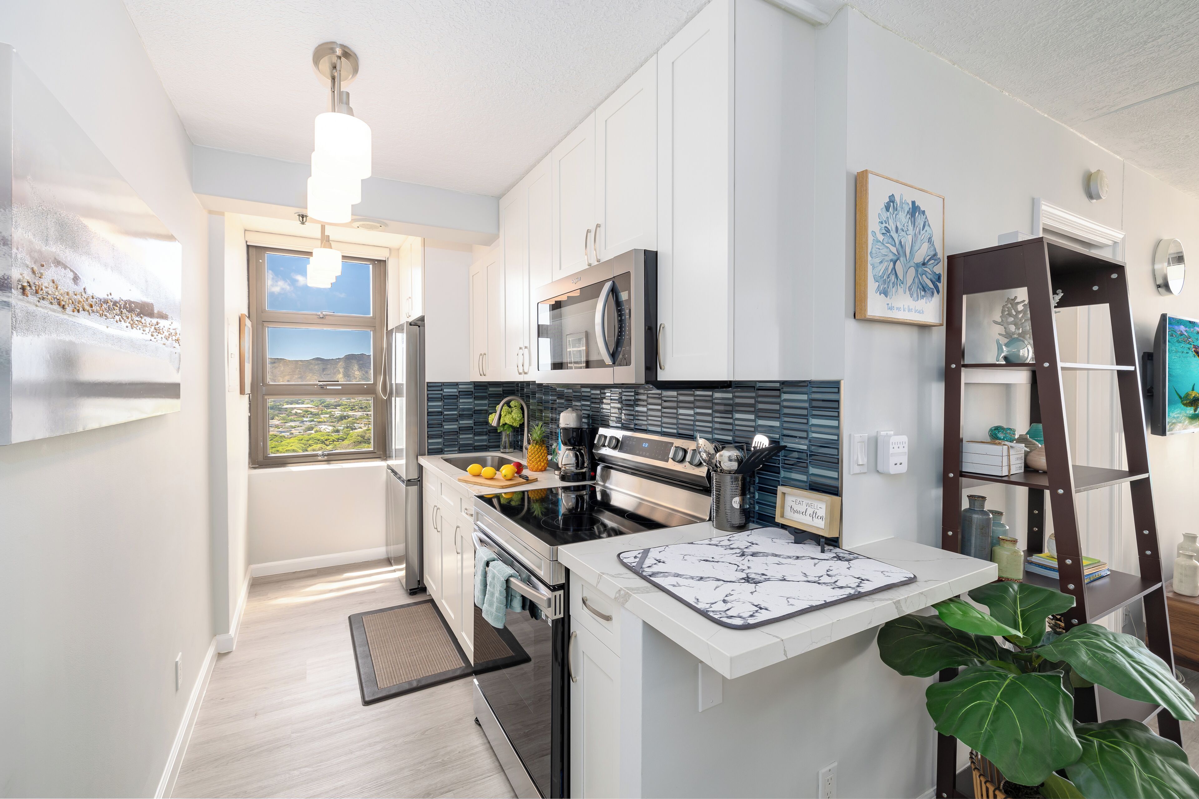 A modern kitchen with white cabinets, a stainless steel stove, and a large window offering a view of the outdoors.
