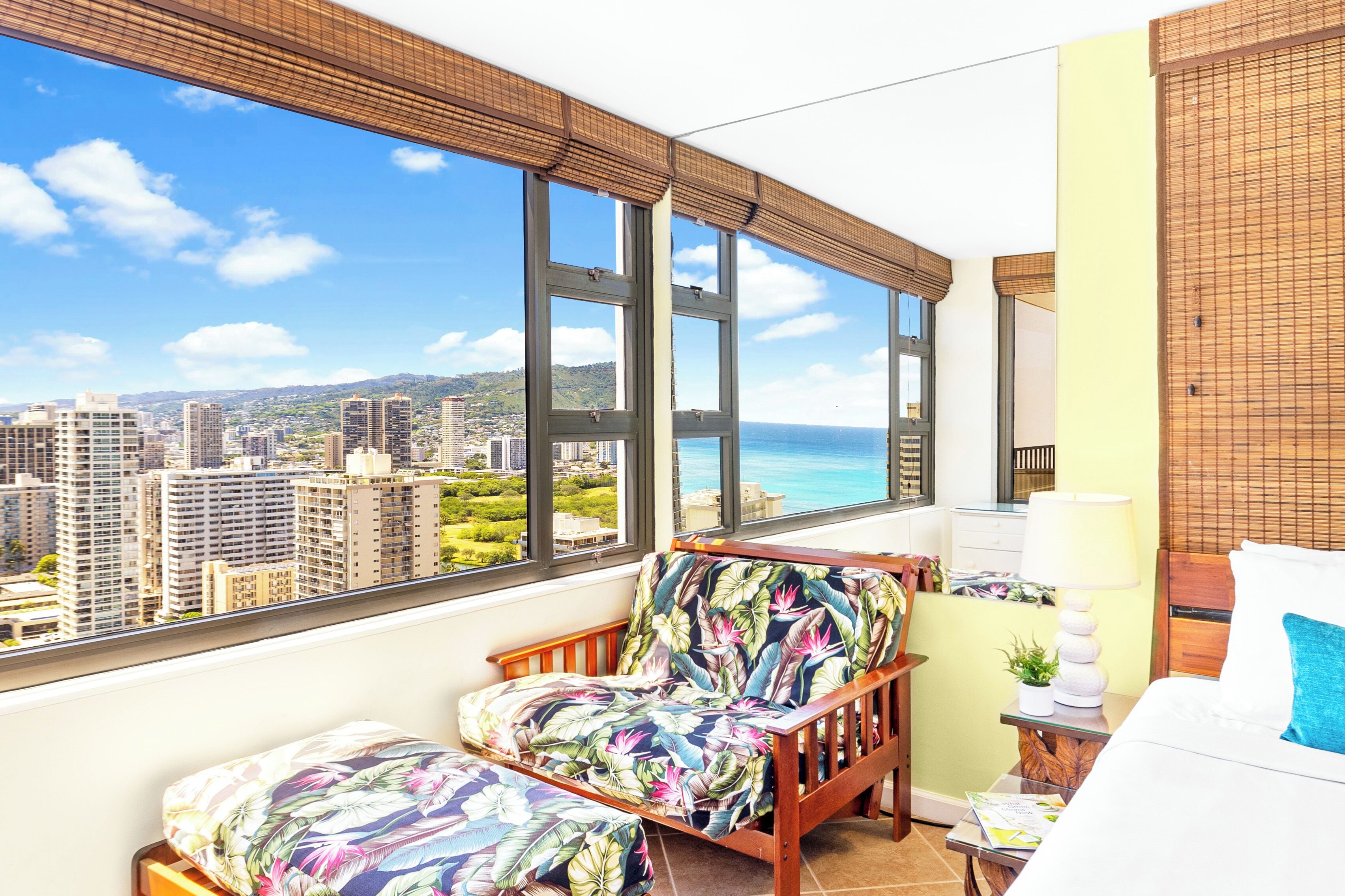 Un balcon avec vue sur la ville, un lit, une chaise et une petite table avec une lampe.