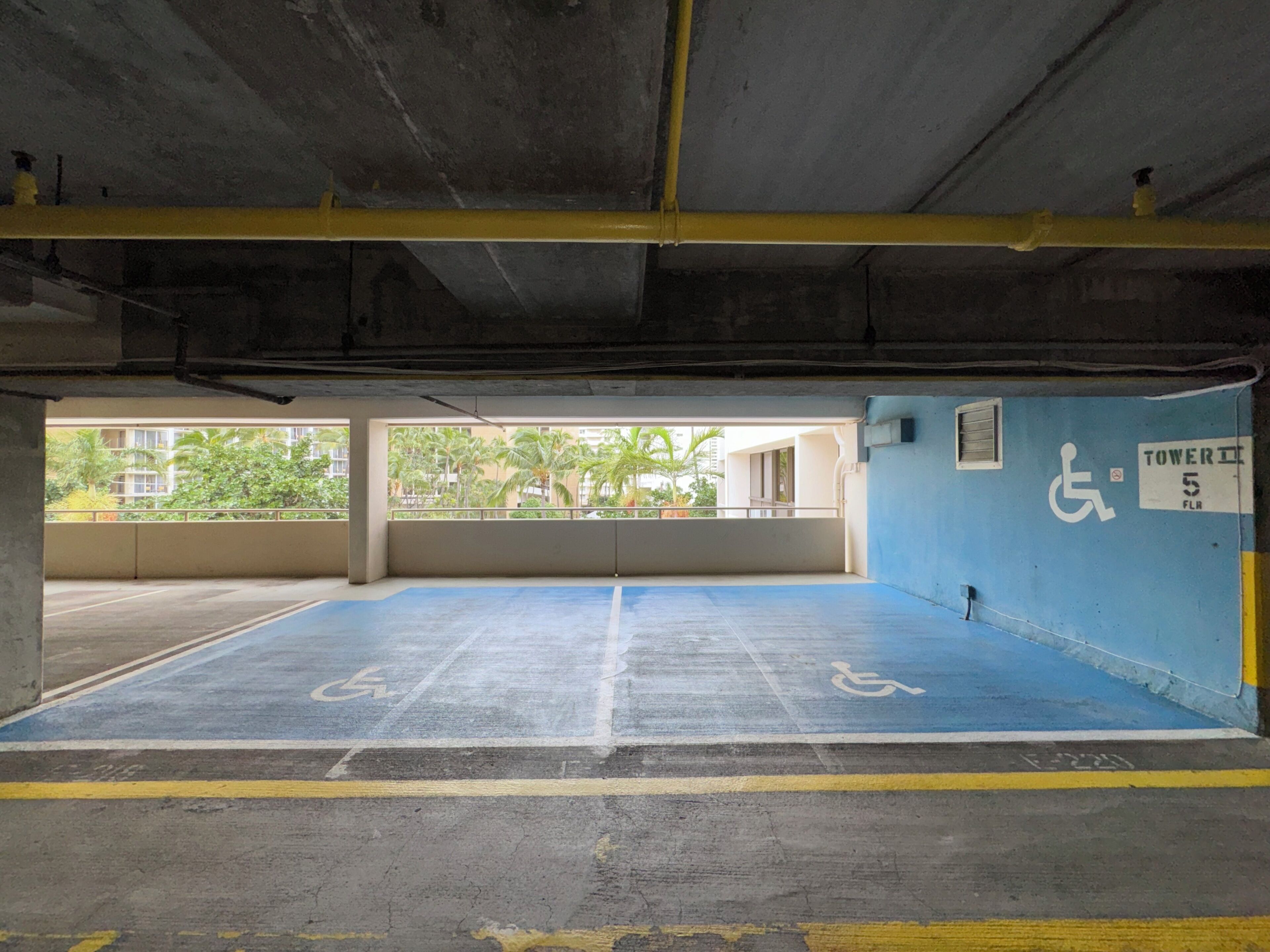 An empty parking garage with blue handicapped parking spaces, a wheelchair accessibility sign, and a sign indicating Tower 5 FLR.
