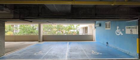 An empty parking garage with blue handicapped parking spaces, a wheelchair accessibility sign, and a sign indicating Tower 5 FLR.