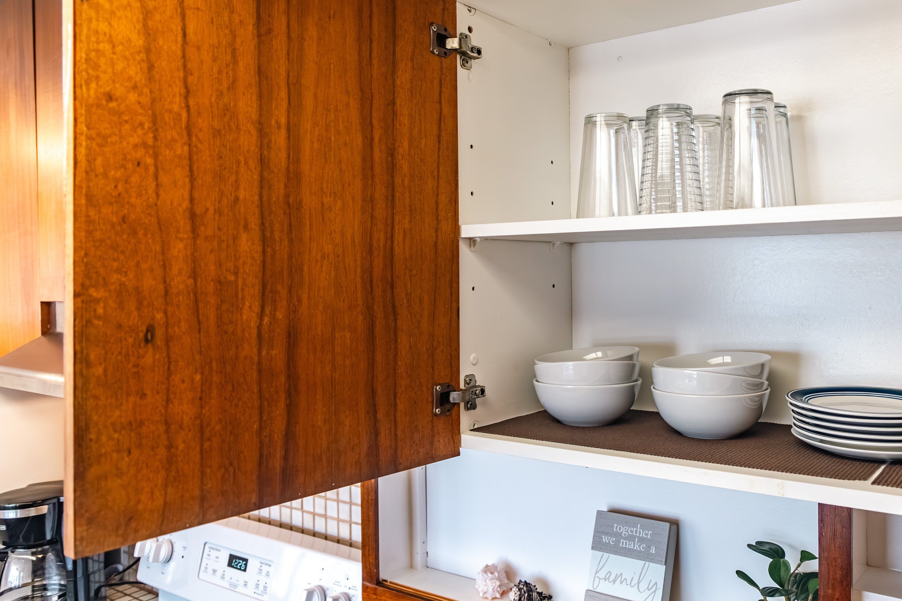 Une cuisine avec des meubles de rangement en bois, un plan de travail blanc et divers ustensiles de cuisine, notamment des bols et des assiettes.