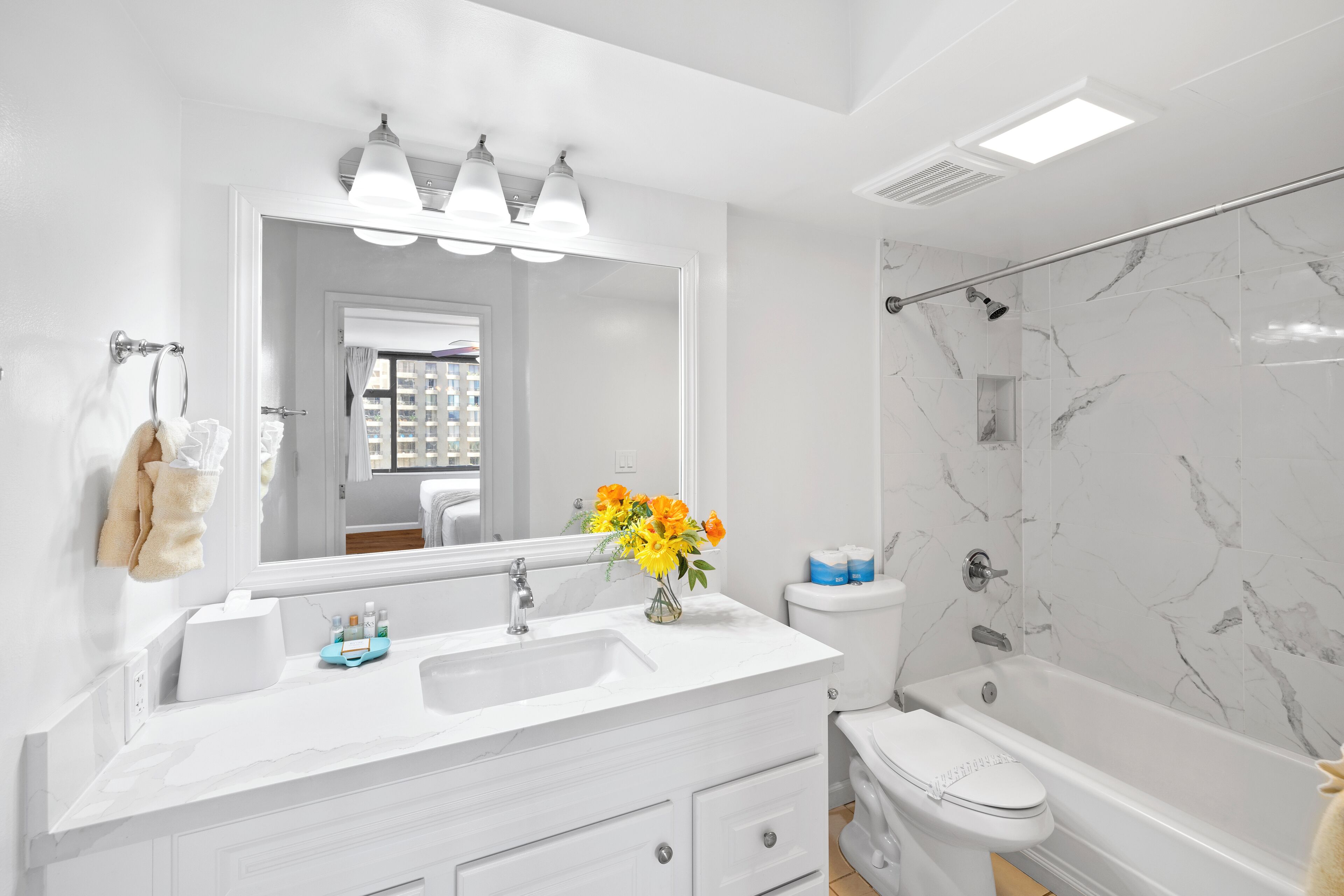 A modern bathroom with a white vanity, a large mirror, a shower with a glass door, and a toilet.