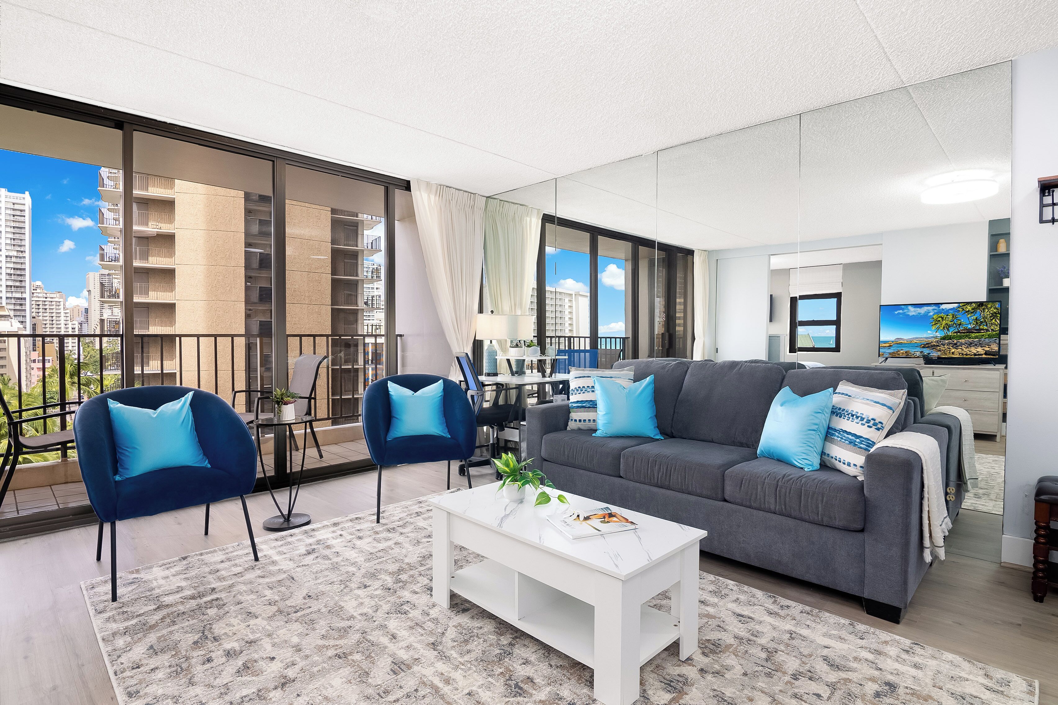 Ein modernes Wohnzimmer mit einem grauen Sofa, blauen Sesseln, einem weißen Couchtisch und einem großen Fenster mit Blick auf die Stadt.