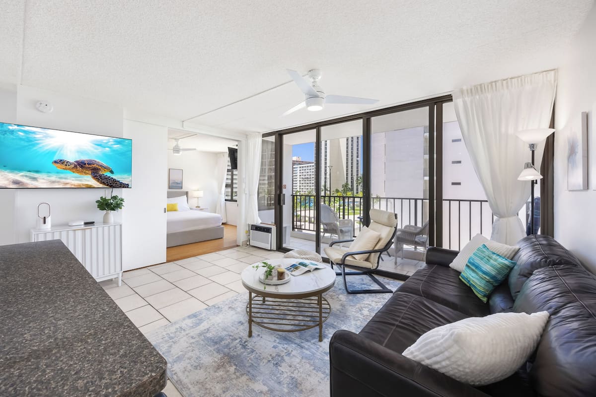 Ein modernes Wohnzimmer mit einer schwarzen Ledersofa, einem runden Couchtisch, einem Flachbildfernseher und einem Balkon mit Blick auf die Stadt.