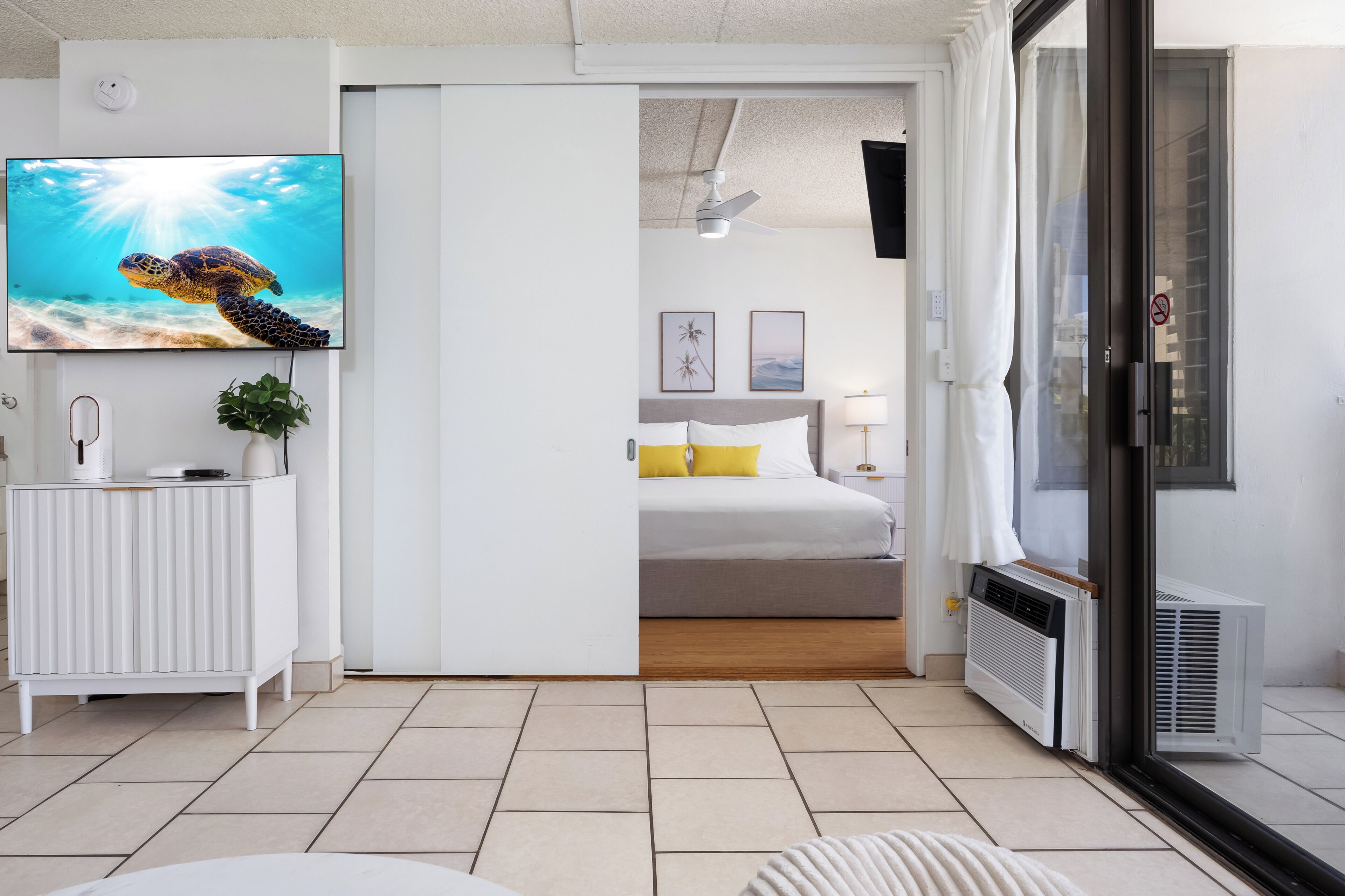 Una habitación de hotel moderna con un televisor grande, una cama, una puerta corredera a un balcón y un radiador.