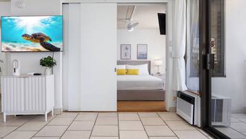 Una habitación de hotel moderna con un televisor grande, una cama, una puerta corredera a un balcón y un radiador.