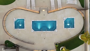 An aerial view of a swimming pool area with three pools, a covered seating area, and a surrounding deck. - Partial Ocean View Condo with King or Queen Bed and Parking (Honolulu)