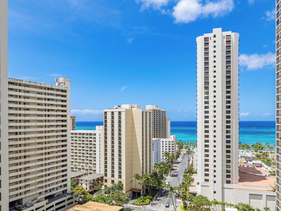 A high-rise hotel with multiple floors, a view of the ocean, and a parking area with cars.