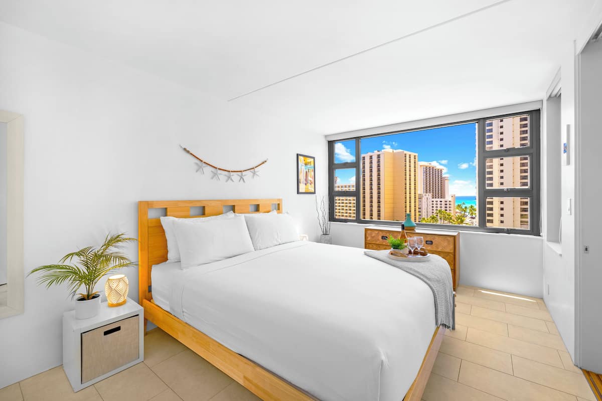 Ein modernes Schlafzimmer mit einem hölzernen Bett, weißer Bettwäsche, einem Nachttisch mit Lampe, einer kleinen Pflanze und einem Fenster mit Blick auf die Stadt.