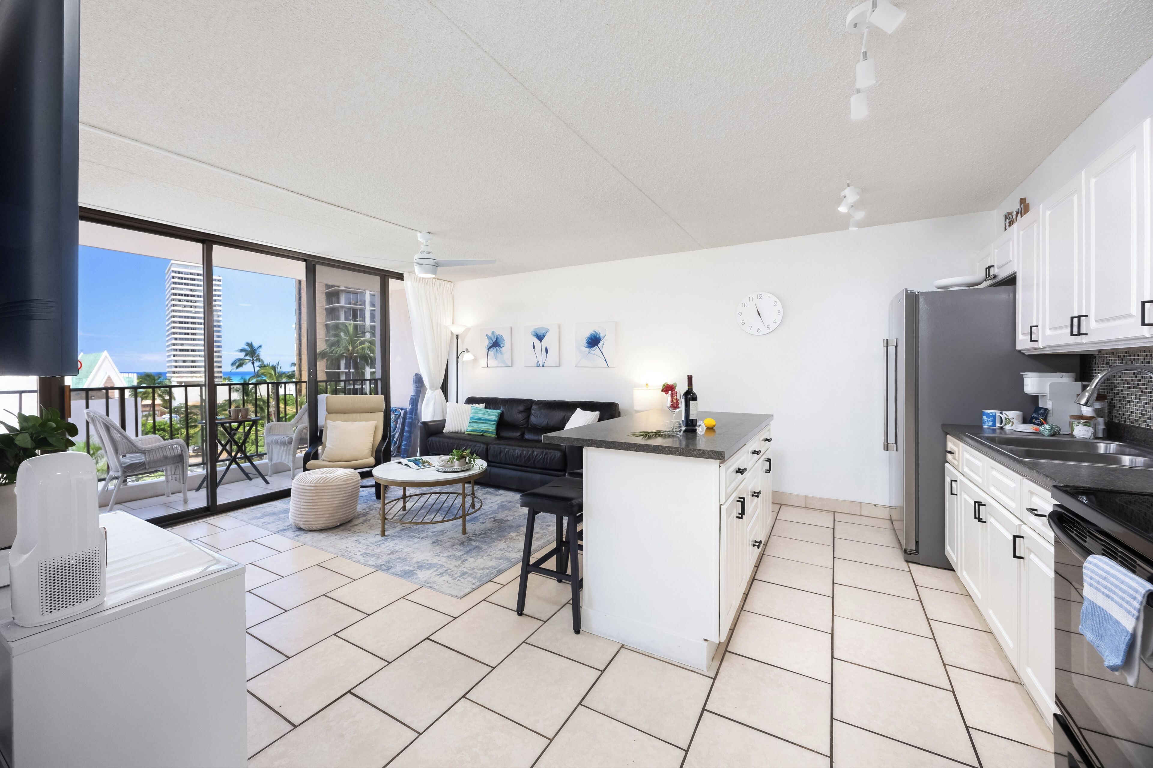 A modern kitchen with white cabinets, a central island, and a dining area with a sofa and chairs.