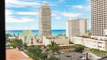 A view of a hotel with a parking lot, a tall building, and a beach in the background.