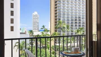 A balcony with a view of tall buildings, palm trees, and a table with cups.