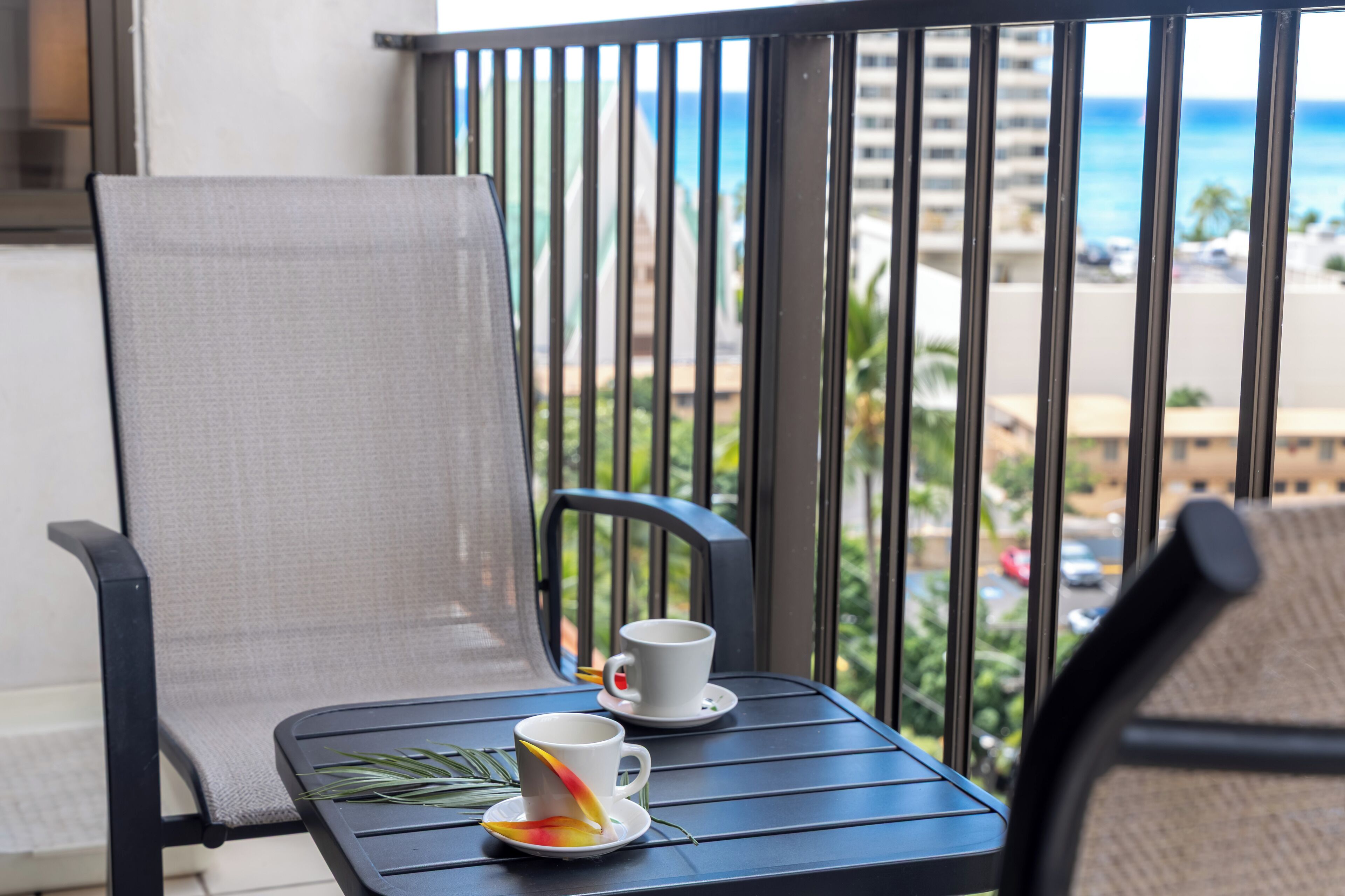 Un balcon avec deux chaises, une table et deux tasses blanches accompagnées de leurs soucoupes.