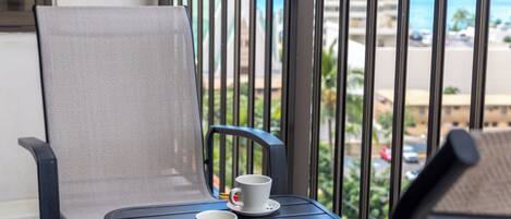 Un balcon avec deux chaises, une table et deux tasses blanches accompagnées de leurs soucoupes.