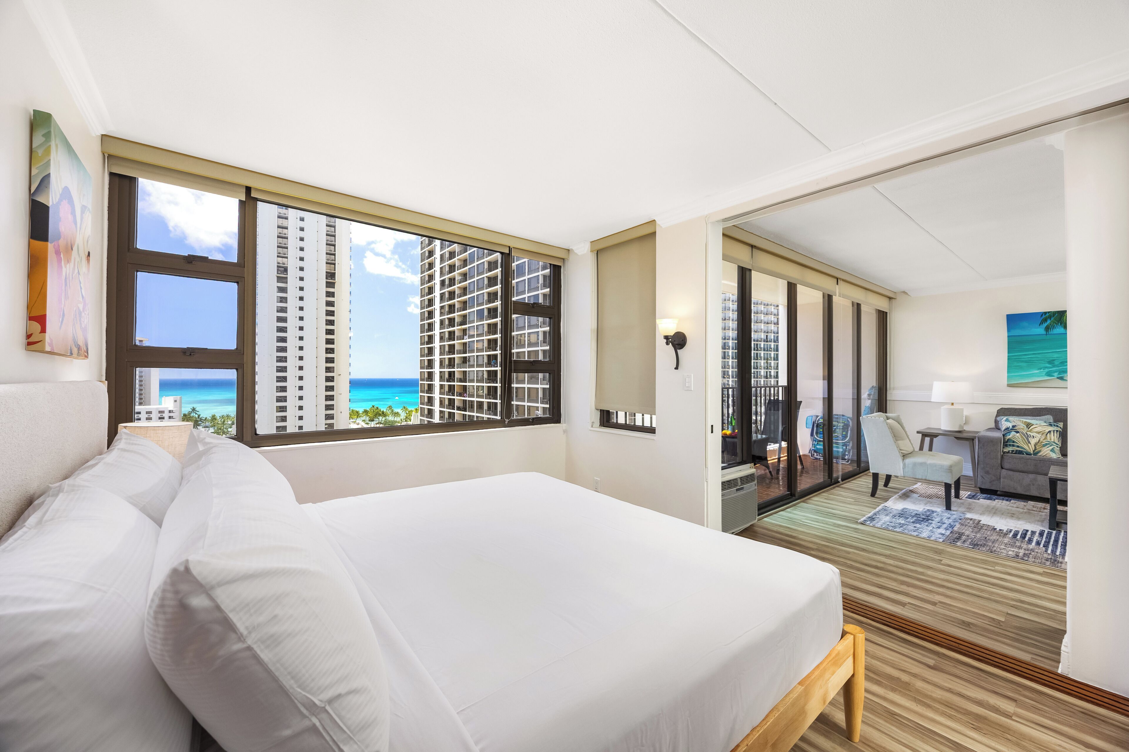 A hotel room with a large bed, a desk, a chair, and a view of the ocean through large windows.
