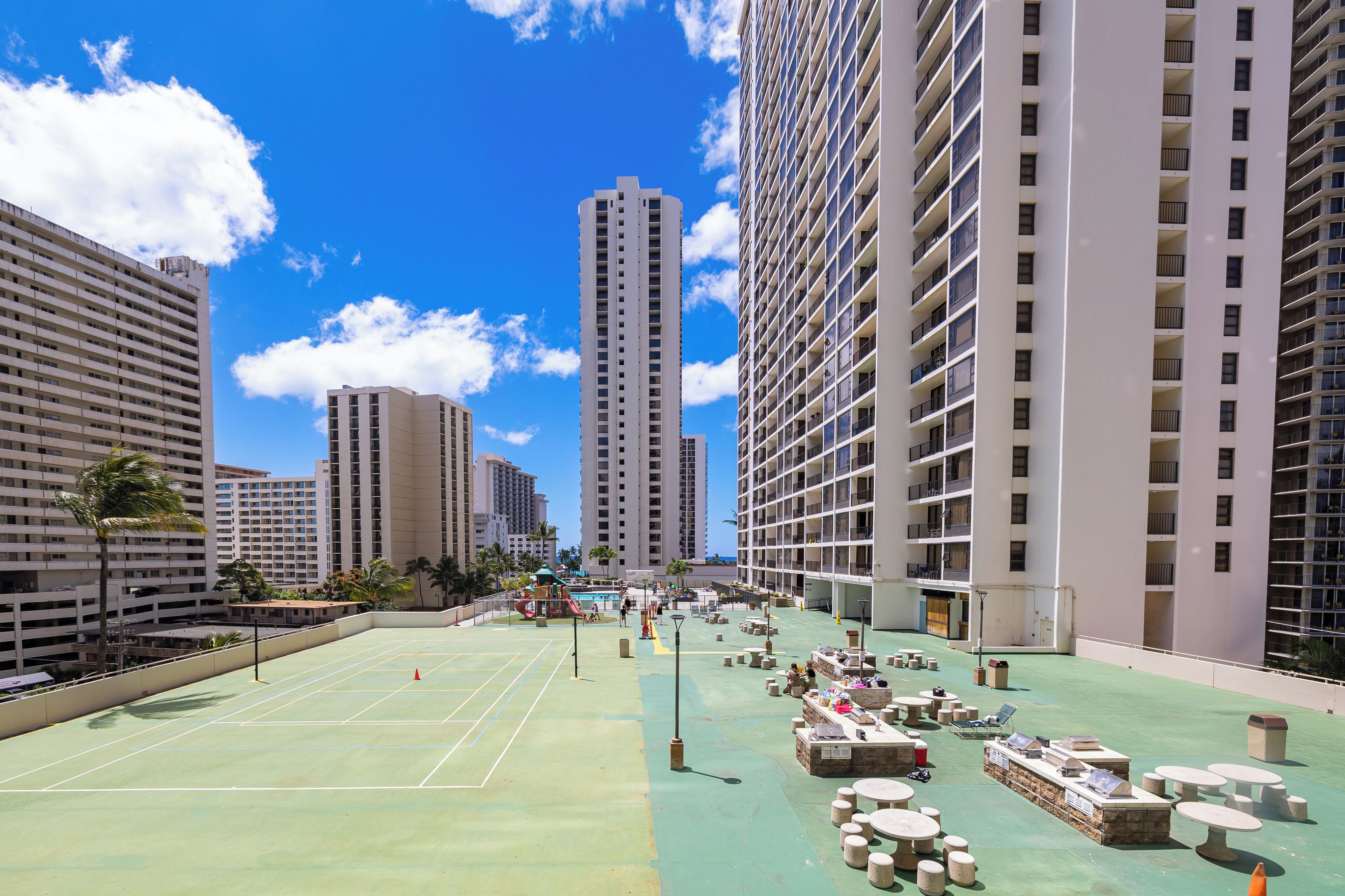 A rooftop tennis court with seating and a water slide.