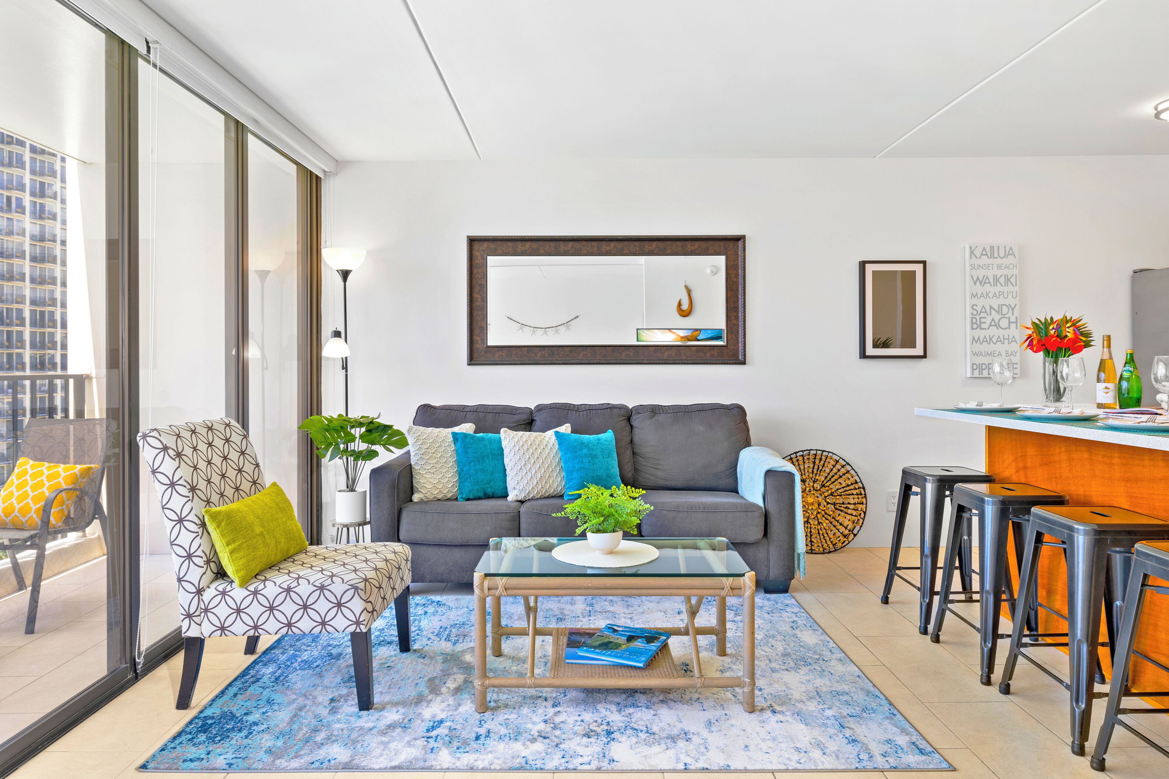 Un salon moderne comprenant un canapé, un fauteuil, une table basse et un coin repas avec des tabourets.