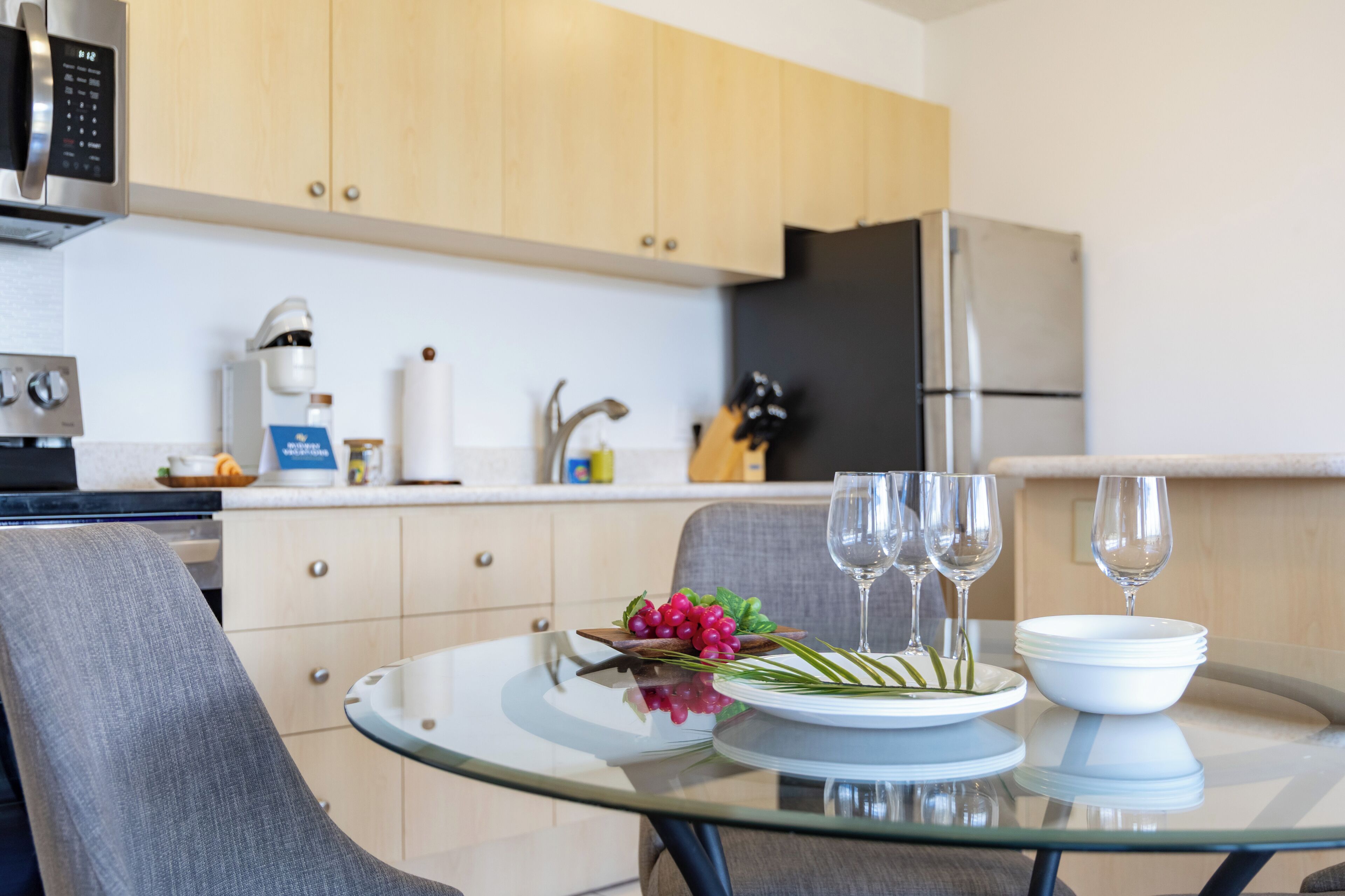 Een moderne keuken met houten kastjes, een roestvrijstalen koelkast en een glazen tafel gedekt met borden, kommen en wijnglazen.