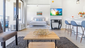 A modern living room with a sofa, a coffee table, and a TV. There is a balcony visible through the glass door. - High Floor Mountain View with King or Queen Bed and Parking (Honolulu)