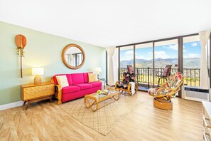 Relax in this serene space with a panoramic mountain view, a vibrant sofa, and a wicker armchair.