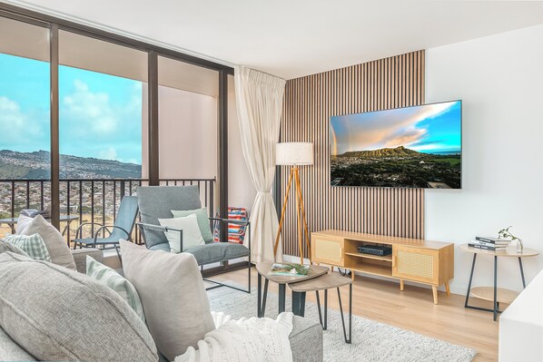 Relax in a spacious living room with a sofa, armchairs, and a flat-screen TV, offering a panoramic view of the surrounding mountains.