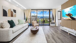 A modern living room with a sofa, coffee table, and a large TV on a wall. - Mountain View Condo with King or Queen Bed and Parking (Honolulu)