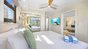 A hotel room with a large bed, a ceiling fan, a TV, and a balcony with a view of buildings. - Mountain View Condo with King or Queen Bed and Parking (Honolulu)