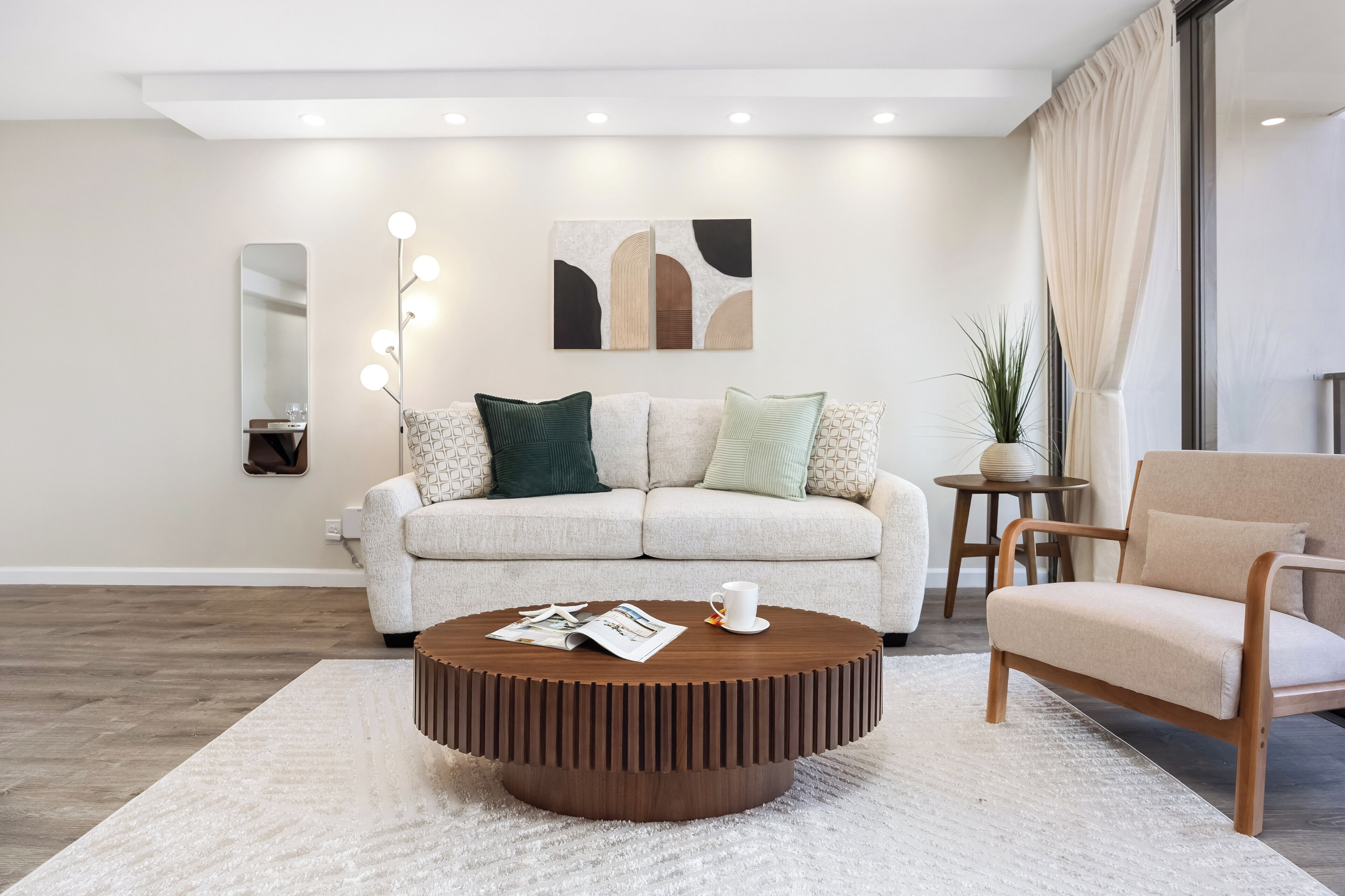 A modern living room with a round wooden coffee table, a sofa, a chair, and a small side table with a plant.