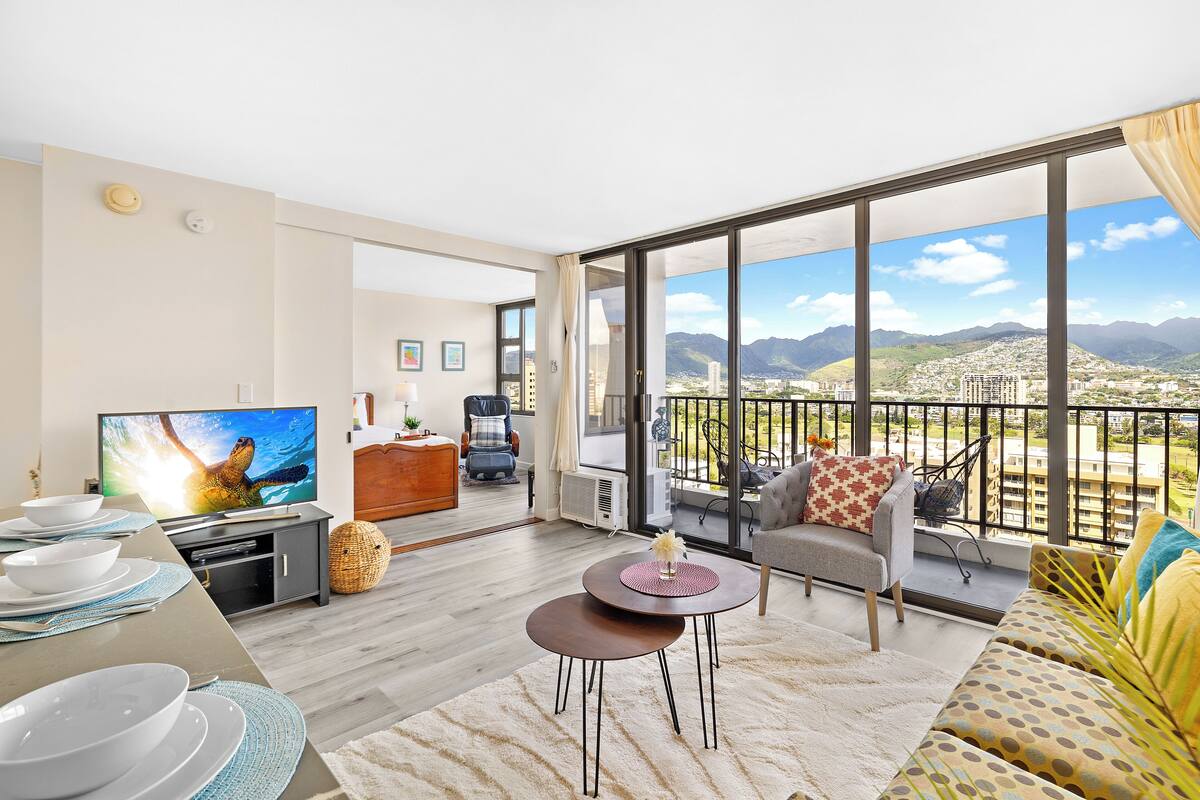 Ein modernes Wohnzimmer mit großem Fernseher, Essbereich und einem Balkon mit Blick auf die Stadt.