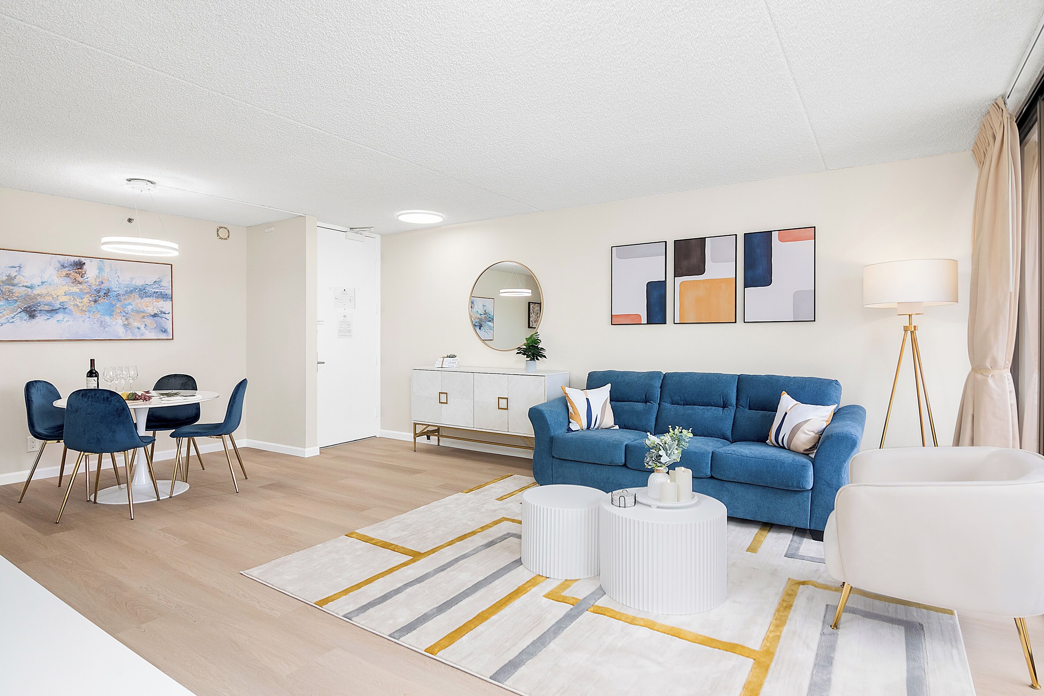 A modern living room with a blue sofa, white coffee table, and a dining area with a table and chairs.