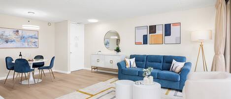 A modern living room with a blue sofa, white coffee table, and a dining area with a table and chairs.