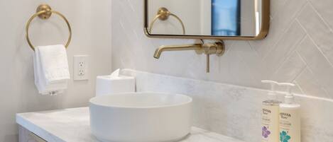 A bathroom with a white sink, gold towel ring, and two bottles of Hawaiian Tropic products on the counter.