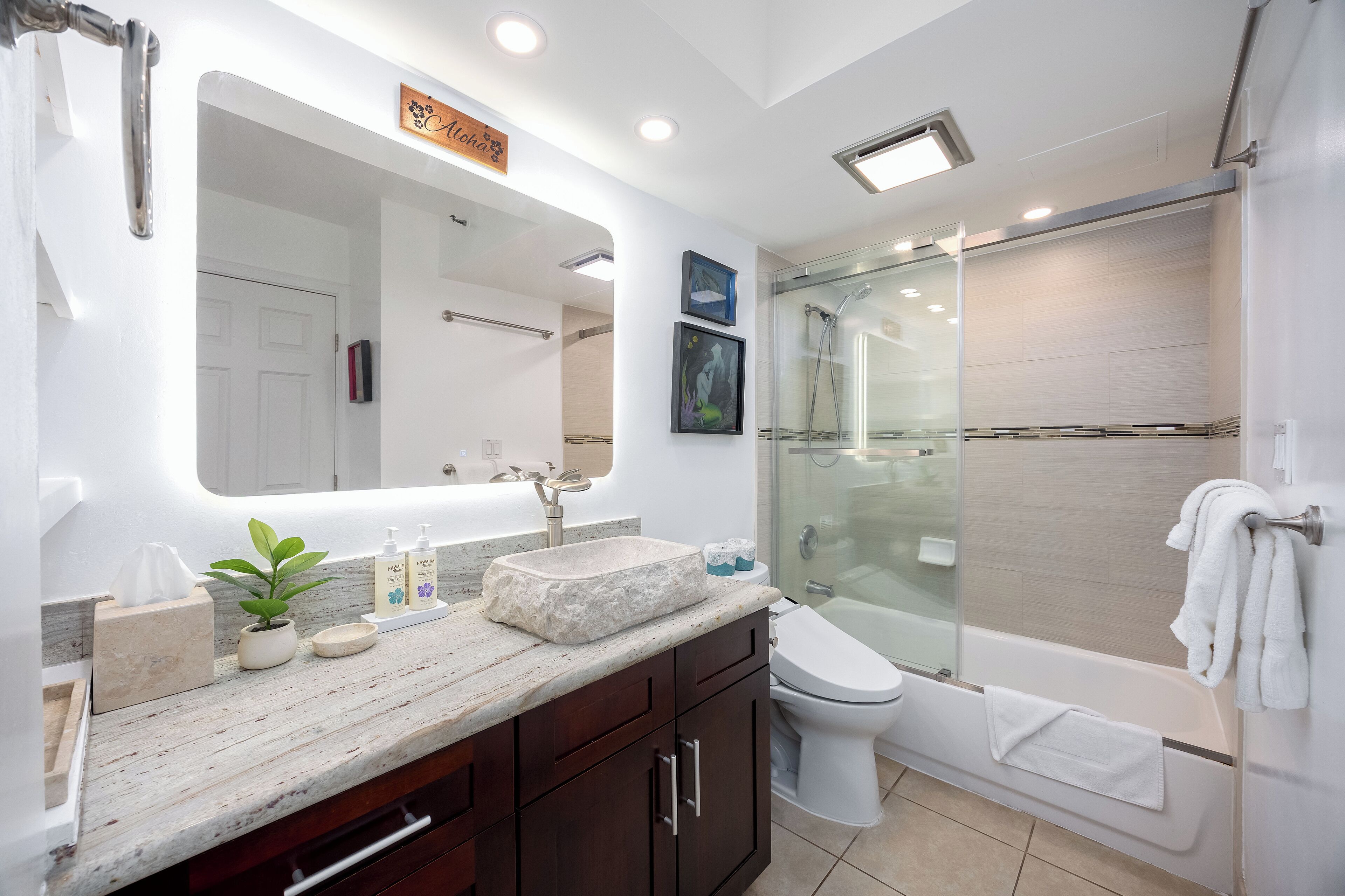A modern bathroom with a glass-enclosed shower, a large mirror, and a marble countertop.