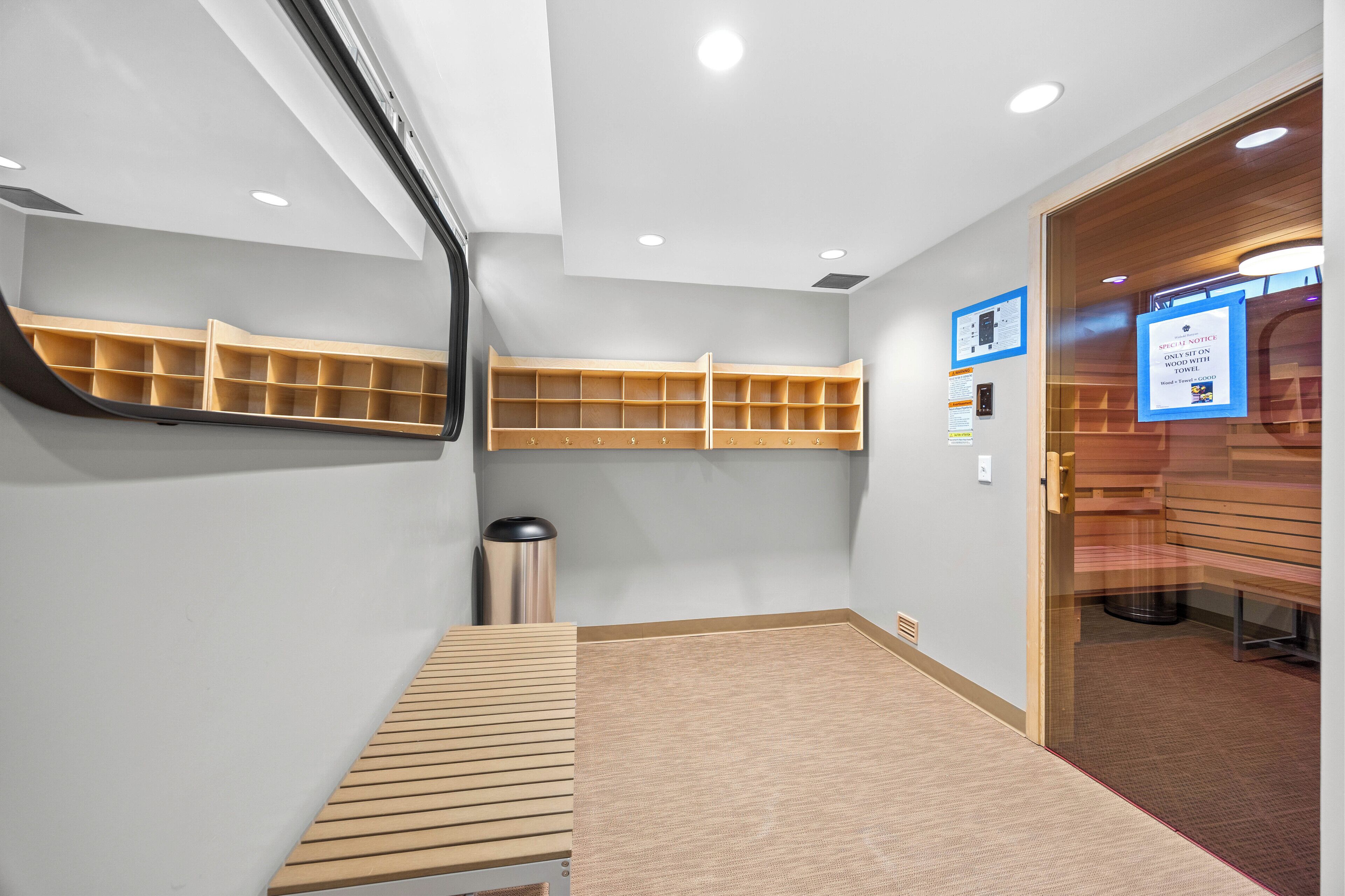 A modern hotel room with built-in wooden shelves, a bench, and a carpeted floor.