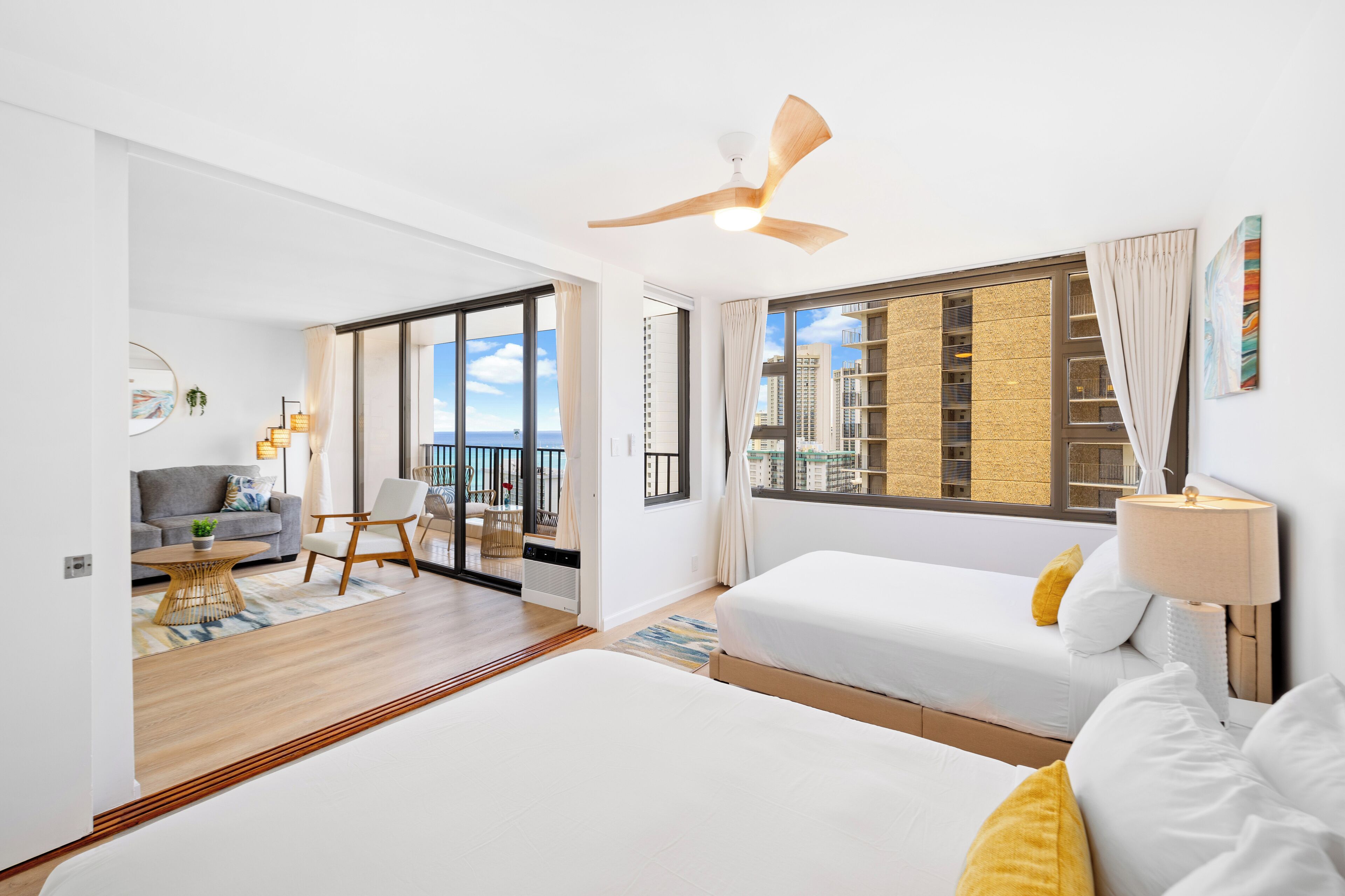 A modern hotel room with a balcony, a sofa, a bed, and a view of the city skyline.