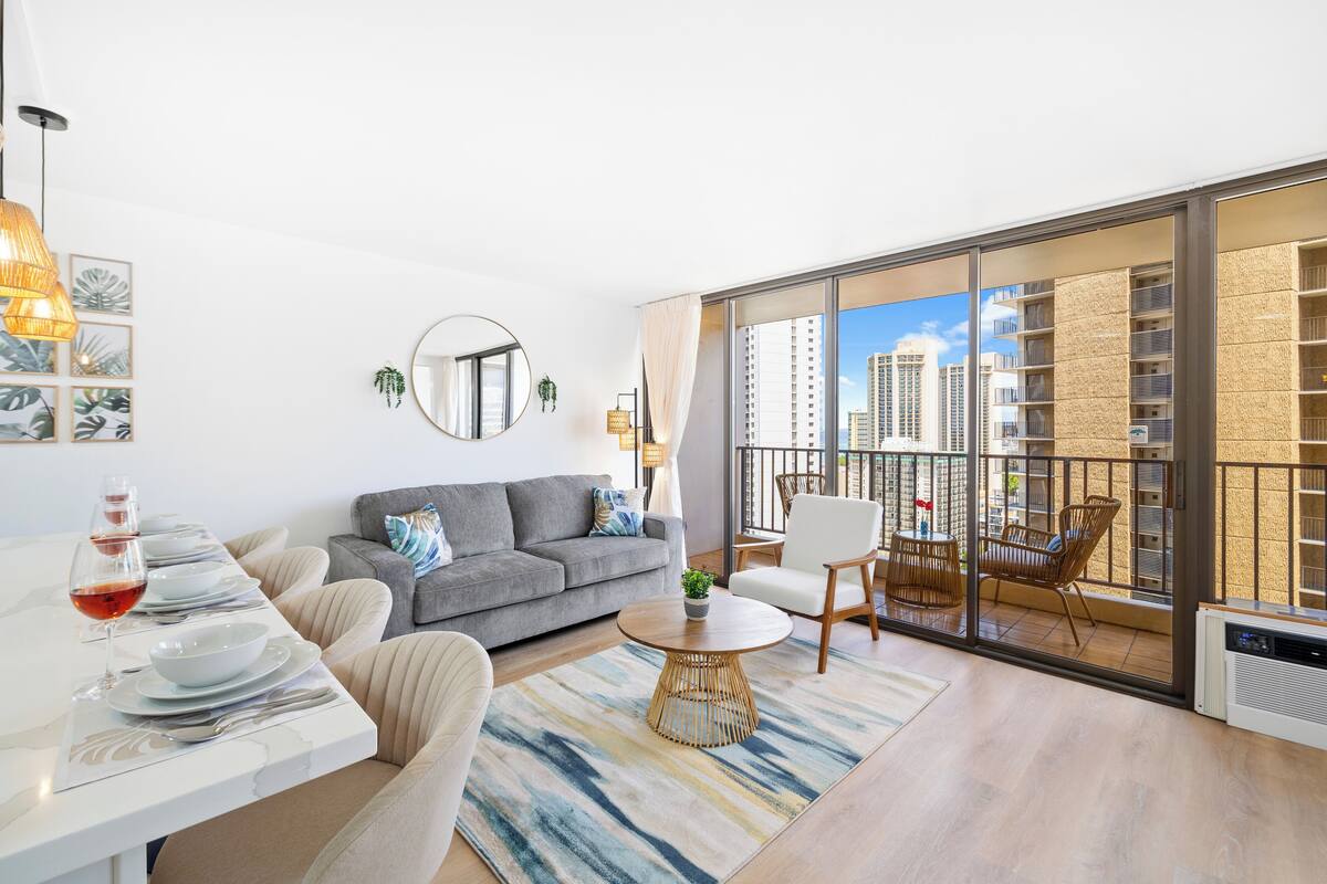 Ein modernes Wohnzimmer mit Essbereich, einem grauen Sofa, einem runden Couchtisch und einem Balkon mit Stadtblick.