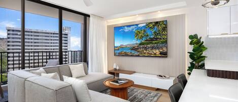 Un salon moderne avec une grande fenêtre, un canapé, une table basse et un tableau représentant une scène de plage.