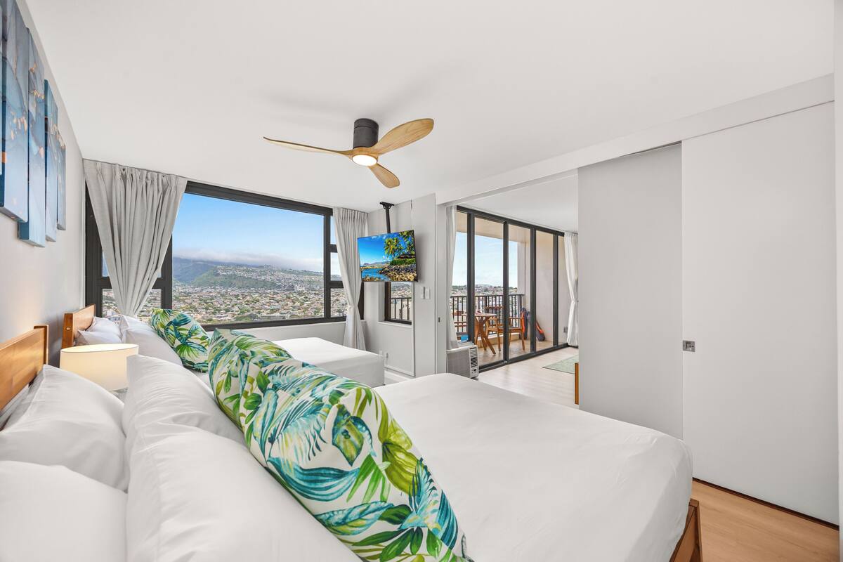 Ein modernes Hotelzimmer mit einem großen Bett, einem Deckenventilator, einem Fernseher und einem Balkon mit Blick auf die Stadt.