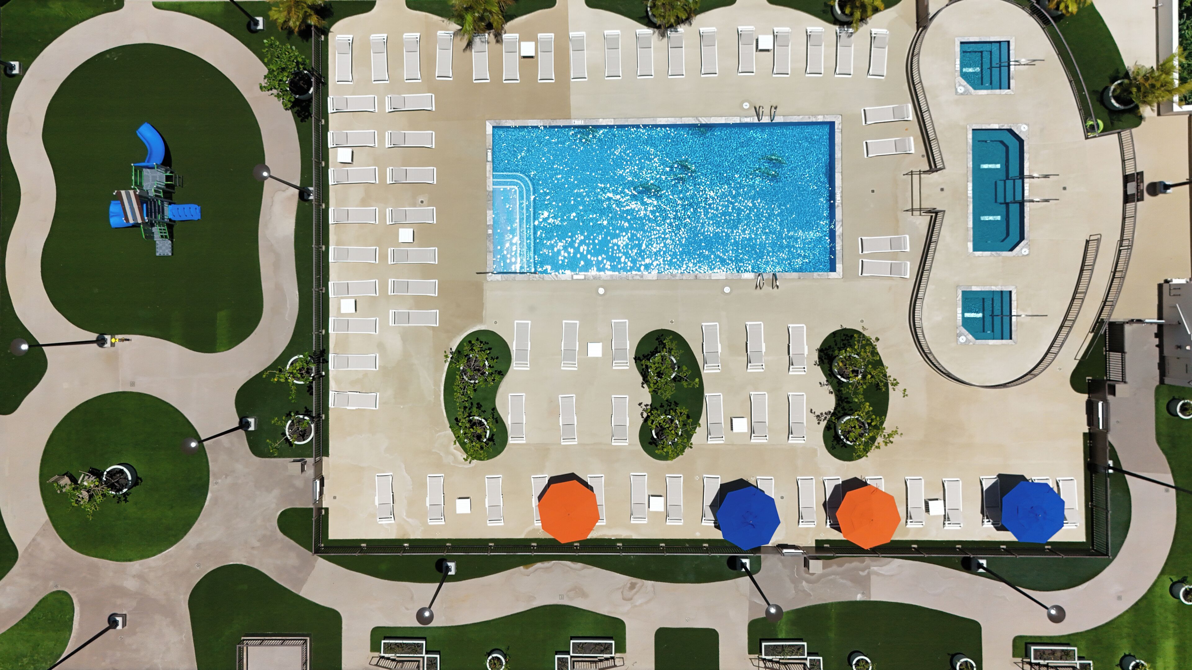 Oversigtsbillede af et hotel med en central swimmingpool, flere loungeområder og grønne områder.