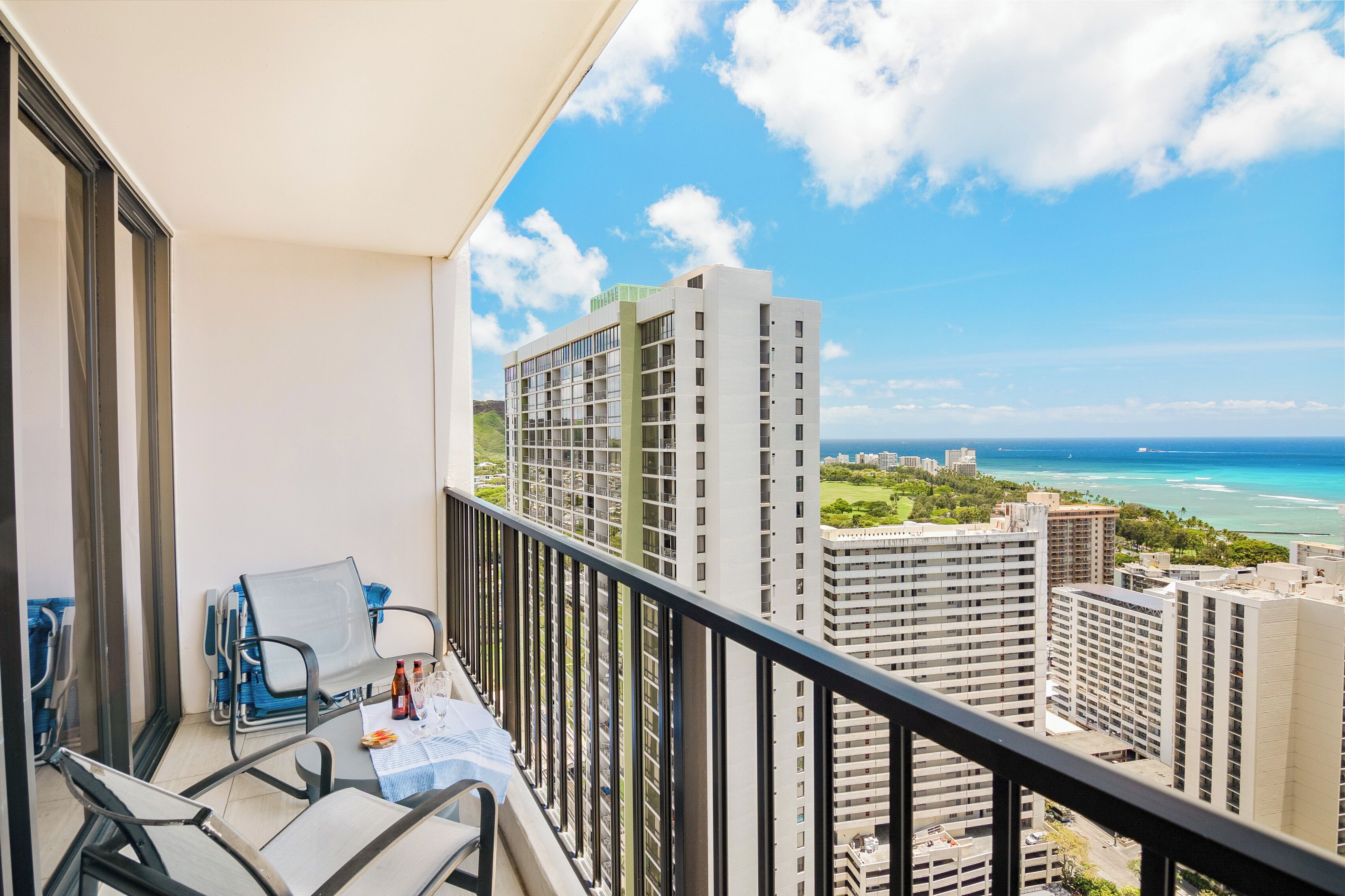 A balcony with a table, chairs, and a view of tall buildings and the ocean.
