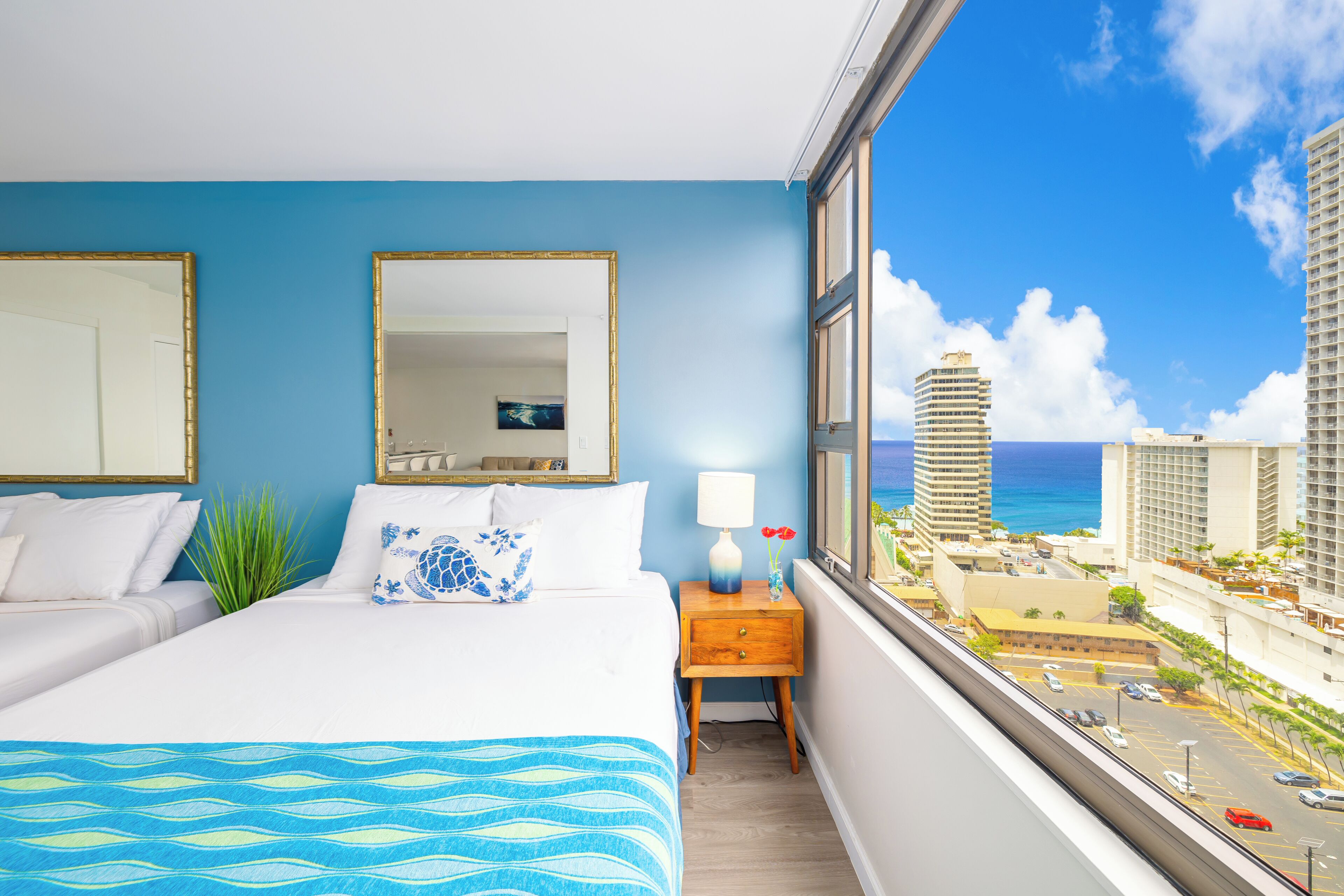 A hotel room with a bed, a nightstand, a mirror, and a window with a city view.