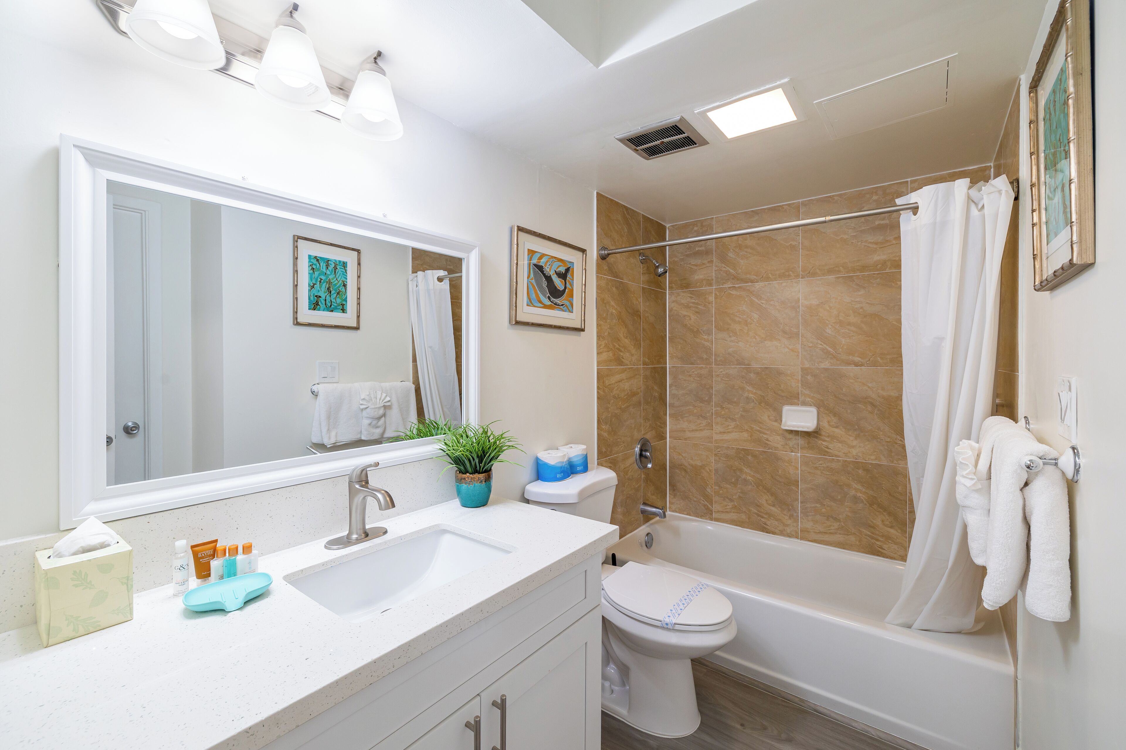A modern bathroom with a sink, toilet, and bathtub. There are towels hanging on the wall, a potted plant on the counter, and a framed picture above the mirror.