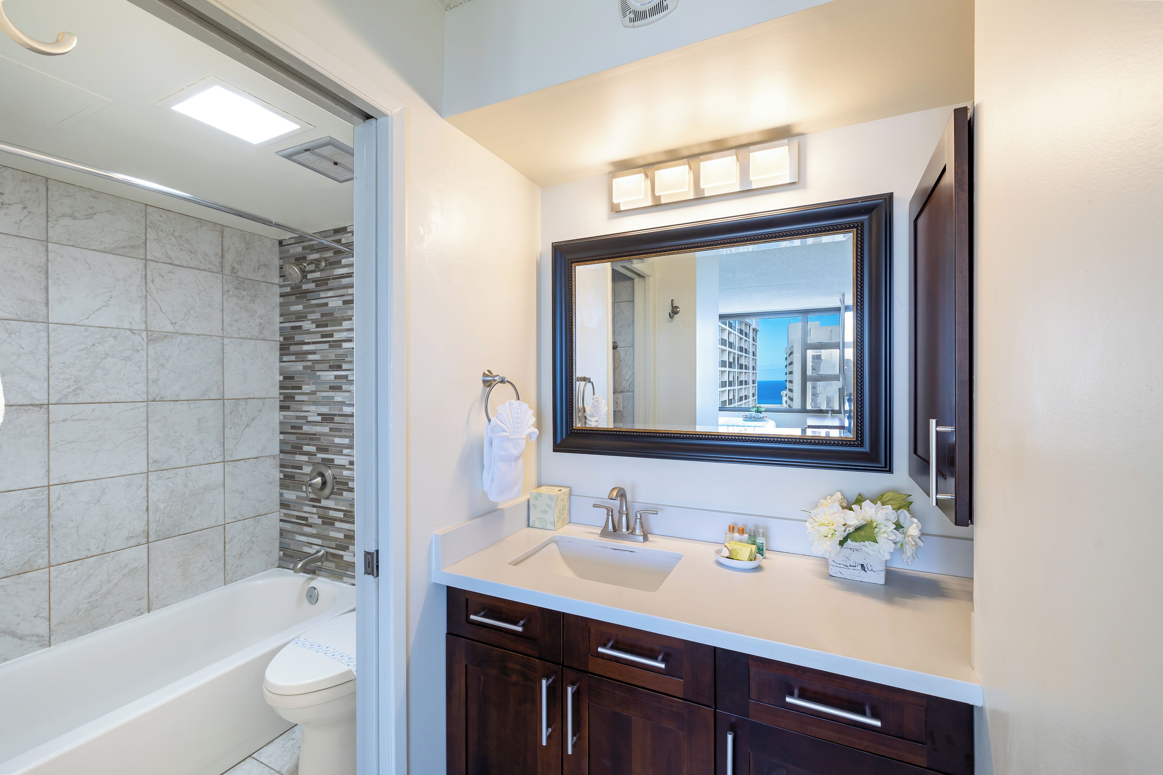 A modern bathroom with a bathtub, toilet, vanity with a sink, and a large mirror.