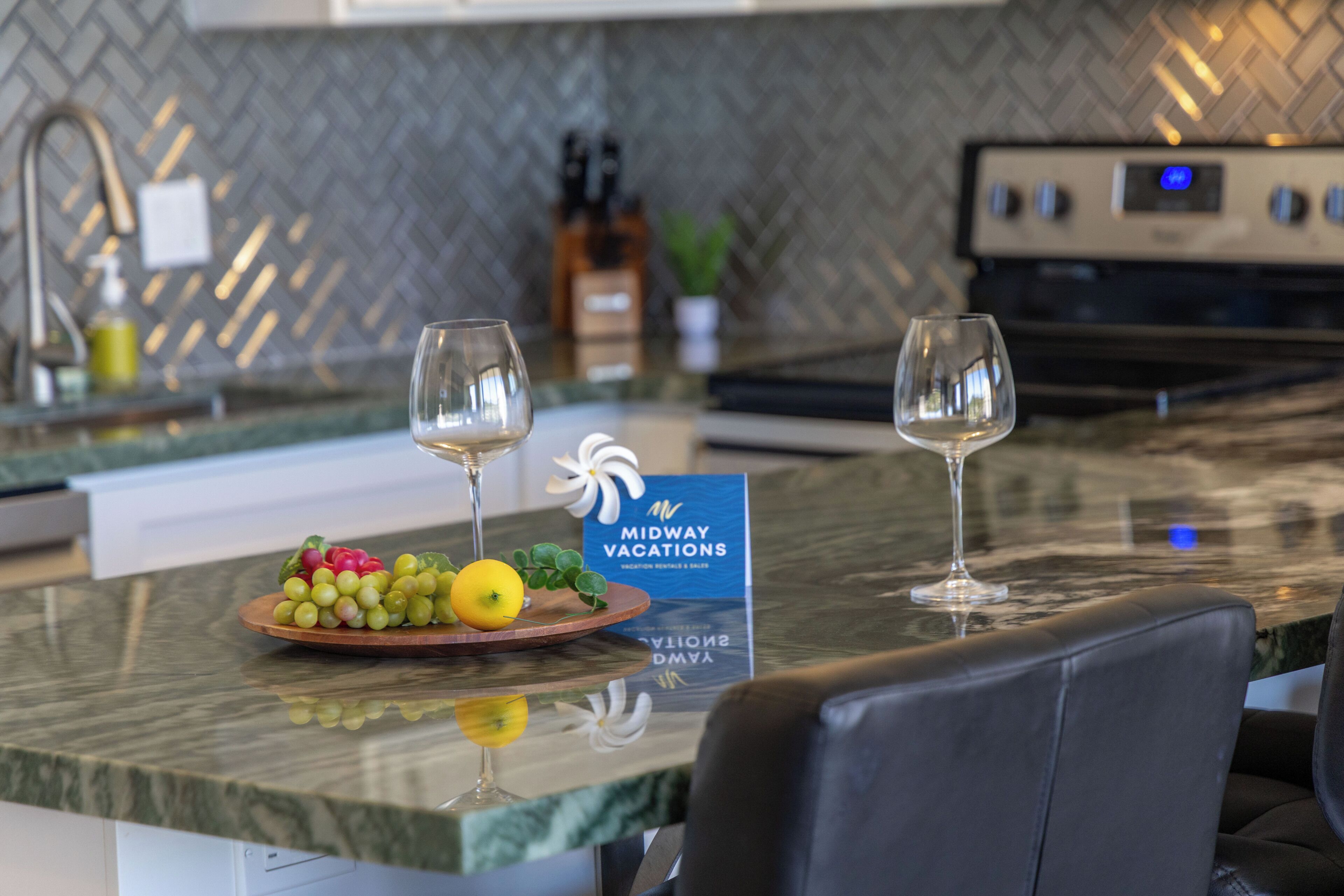 Eine moderne Küche mit Marmorarbeitsplatte, zwei Weingläsern, einer Obstplatte und einem Schild für Midway Vacations.