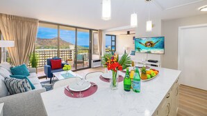 A modern living room with a large TV, dining area, and a balcony with a mountain view.