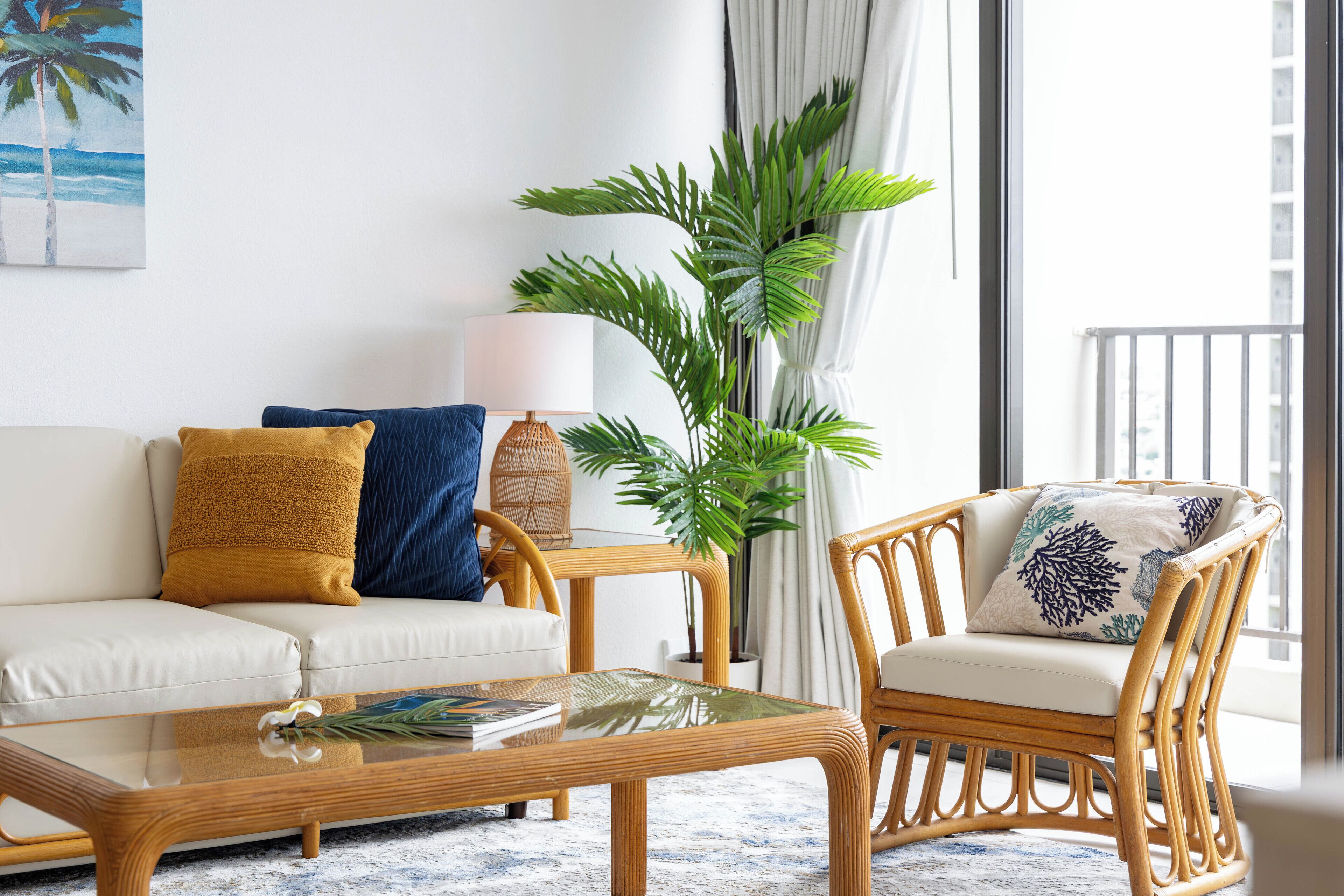 A living room with a white sofa, a wicker chair, a glass coffee table, and a large plant.