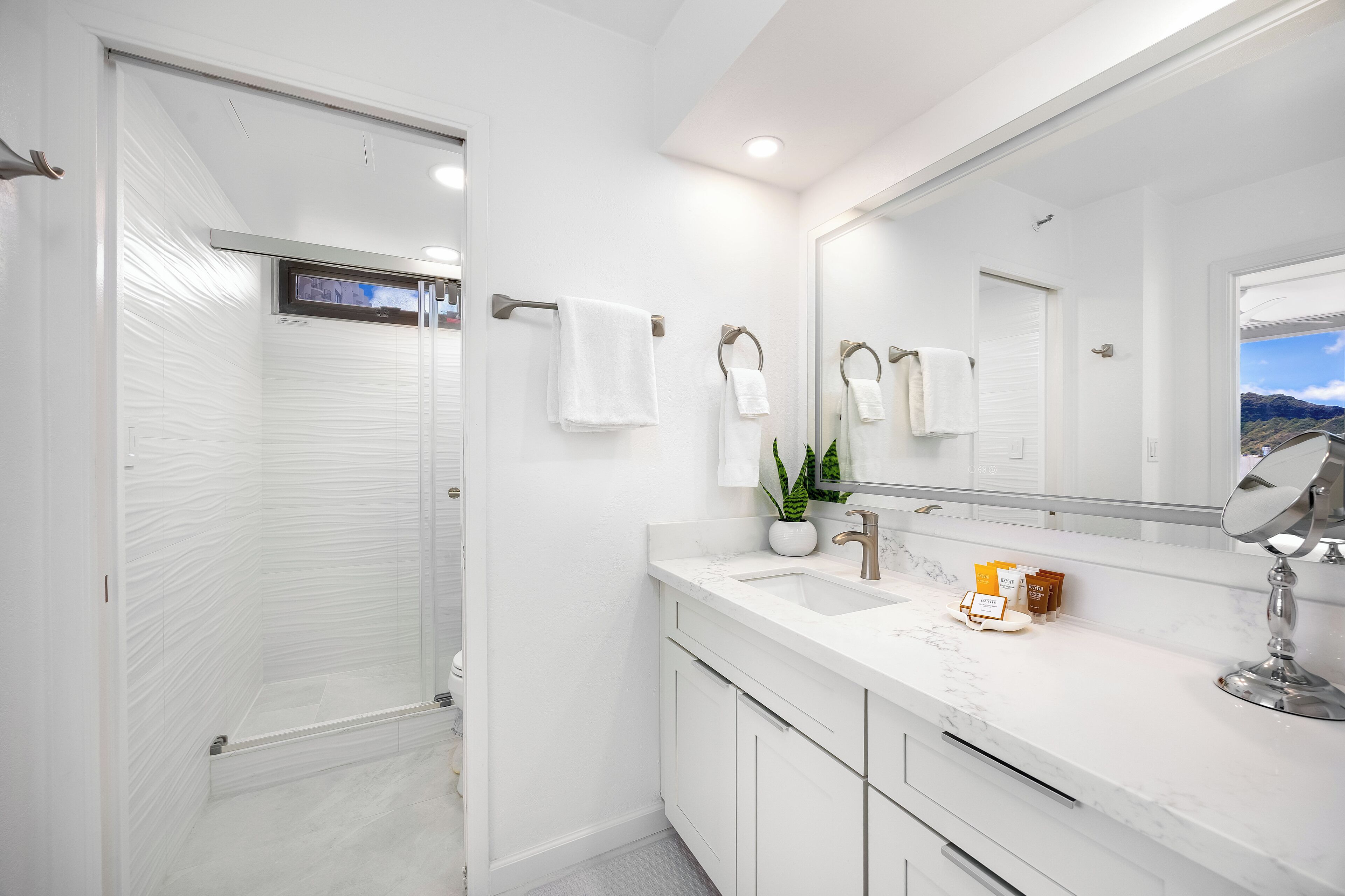 Un baño moderno con cabina de ducha, un espejo grande y un tocador blanco con encimera de mármol.