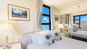 A hotel room with a bed, bedside tables, lamps, a mirror, and a large window with a view of mountains.
